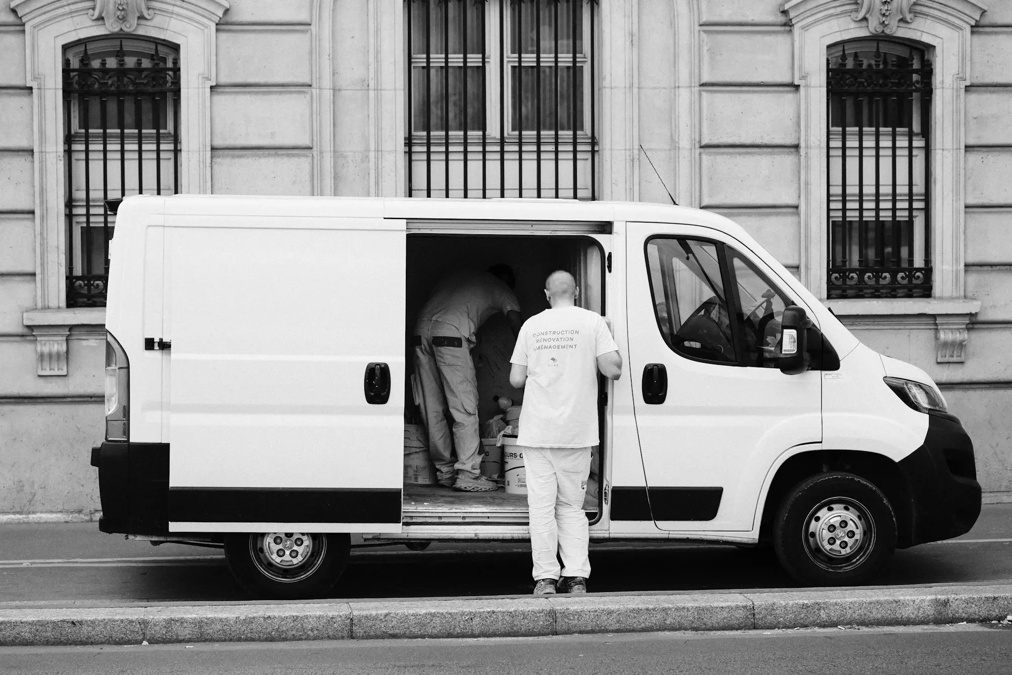 Worker loading goods through the open side door of a white delivery van parked on a street