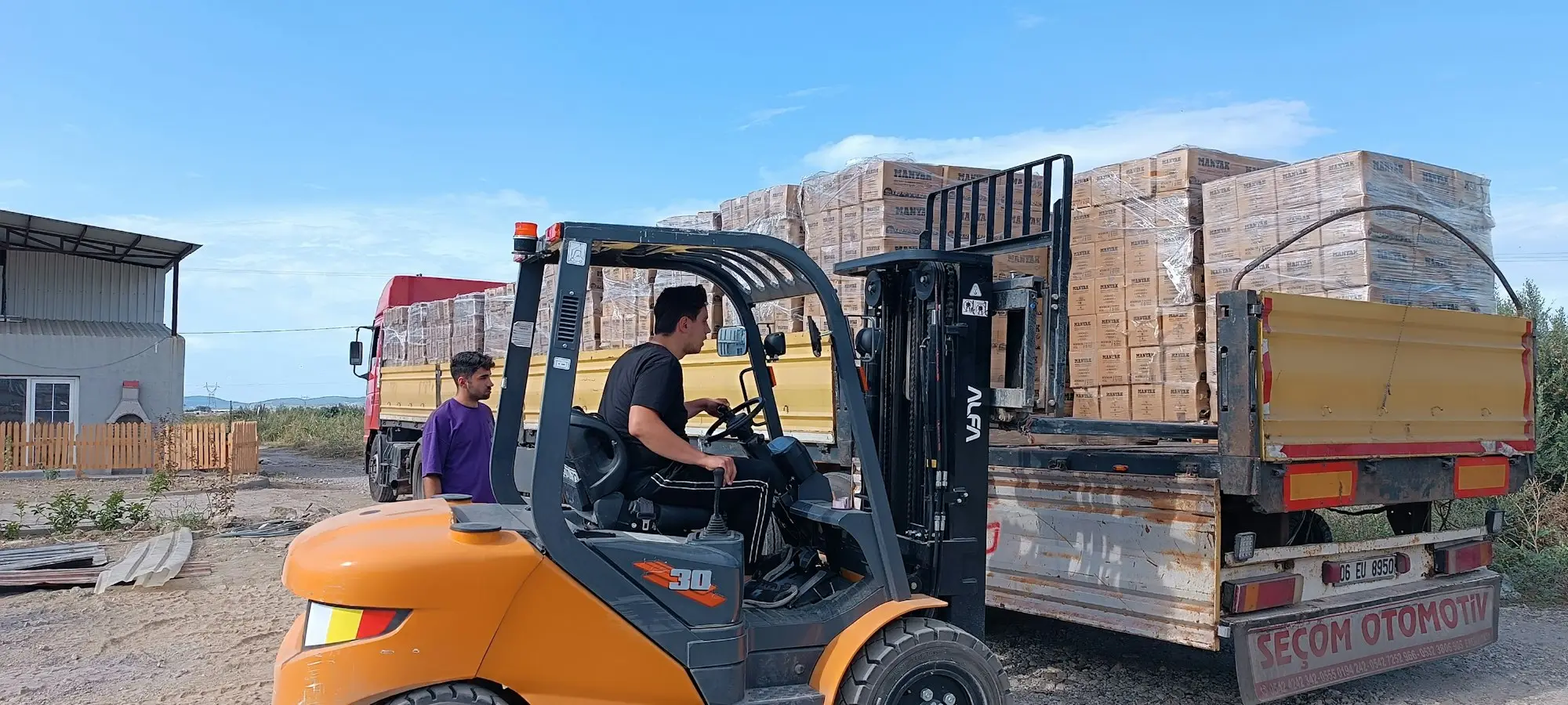 Forklift loading stacked pallets of bricks onto the tray of a truck outdoors