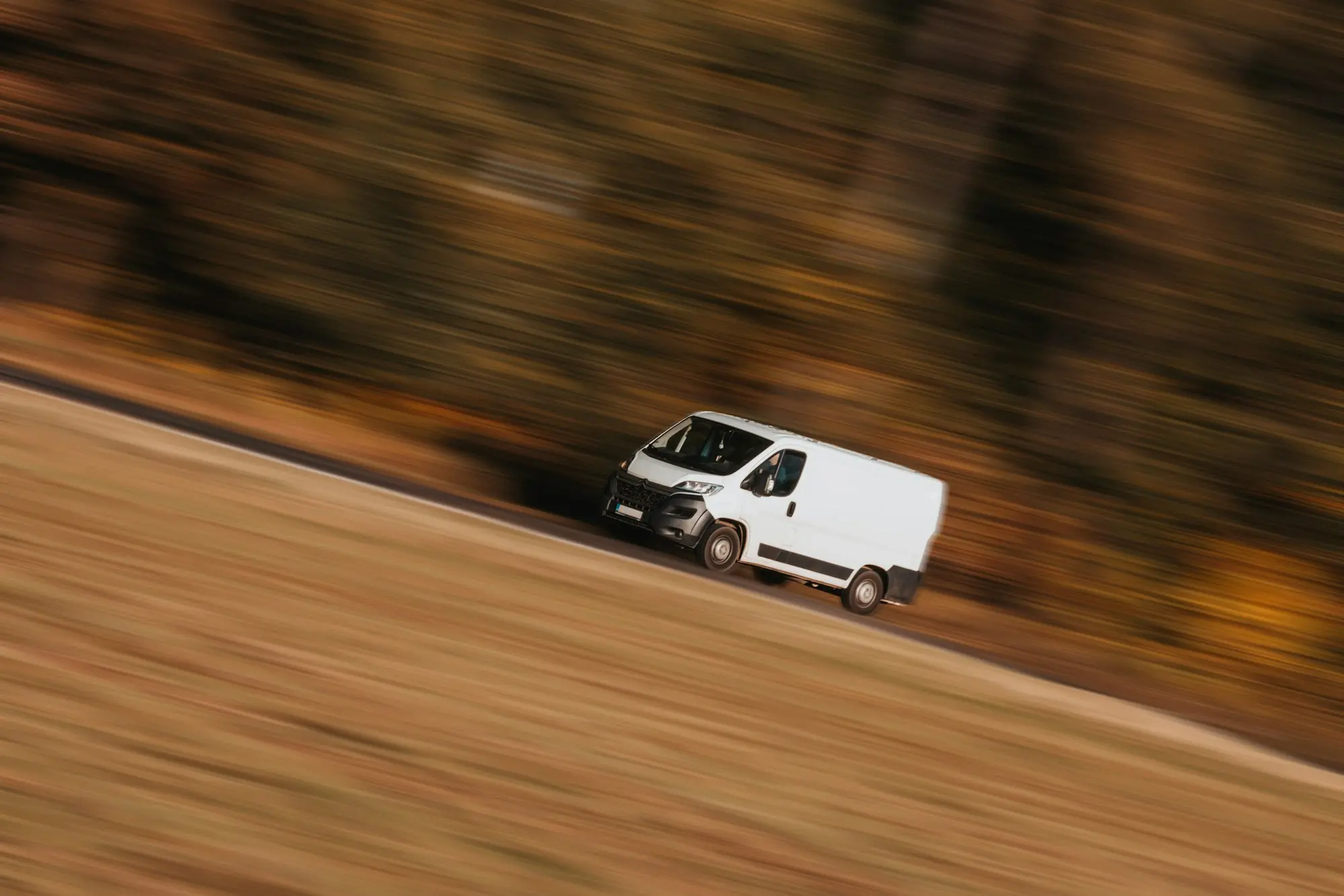White van travelling fast along a country road, blurred with motion