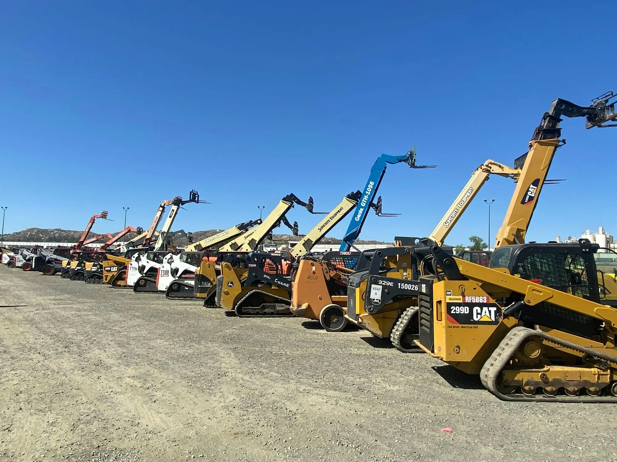 Row of yellow loaders, telehandlers and construction machines parked in a dusty yard