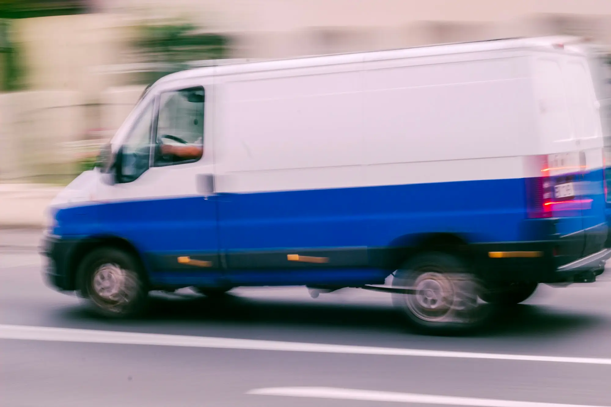 White panel van with a blue lower stripe driving along a city road