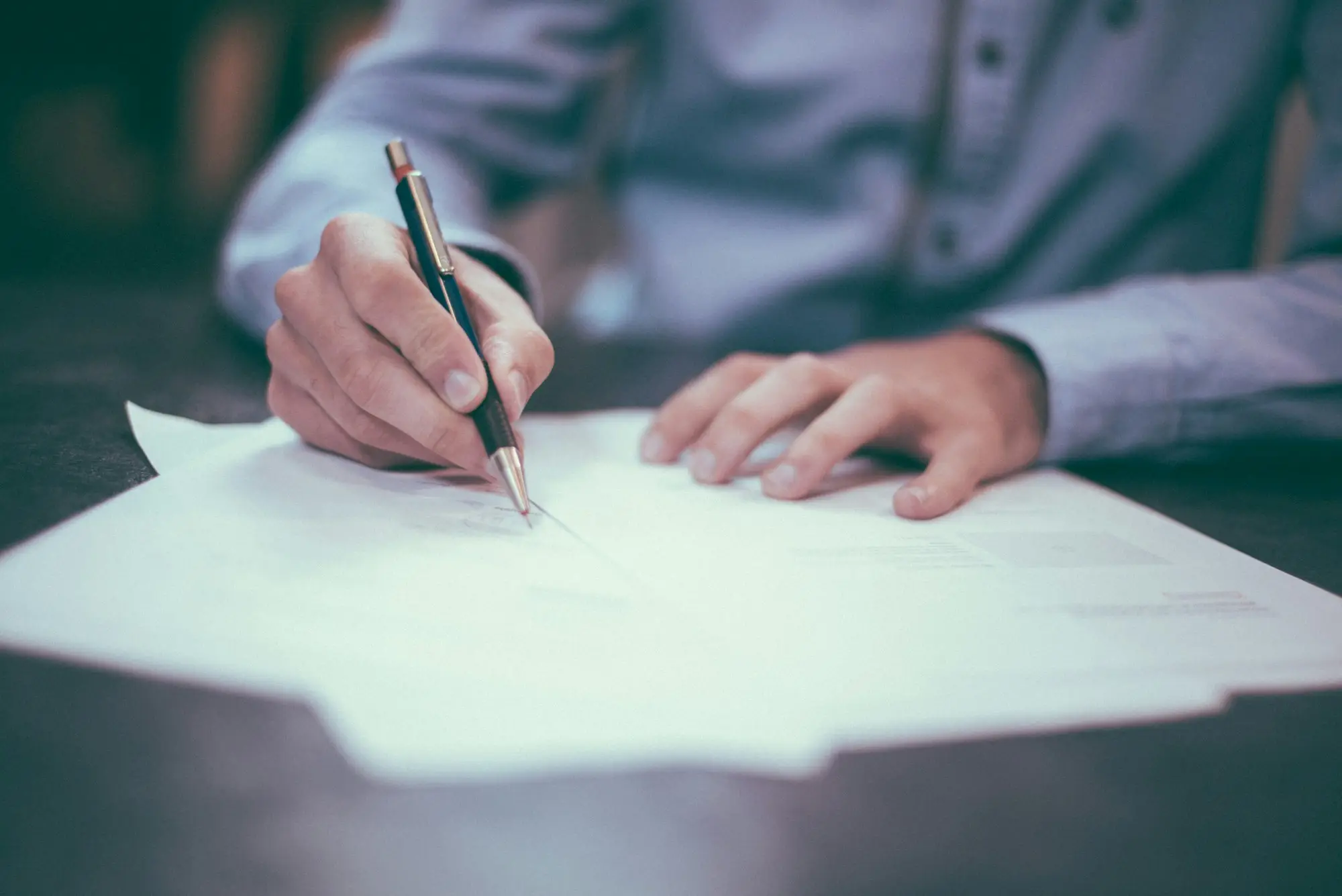 Person in a business shirt signing a document with a pen at a desk
